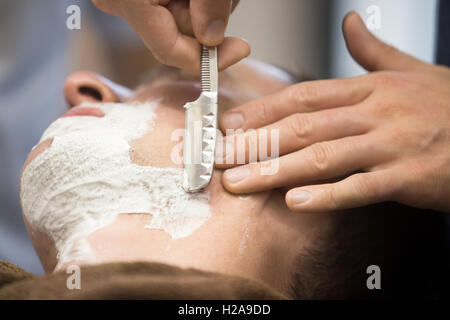 Tourné de l'intérieur de processus de travail moderne dans un salon de barbier. Close-up portrait of beau jeune homme se raser la barbe avec straig Banque D'Images