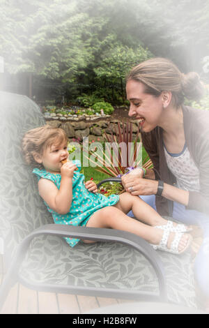 Jeune fille de dix-huit mois, une barre granola manger dehors avec sa mère joyeusement la taquiner, à Issaquah, Washington, USA Banque D'Images