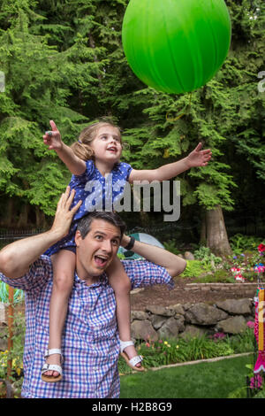 Trente-quatre ans, père tenant sa fille de trois ans alors qu'elle attrape un ballon lancé à sa Banque D'Images