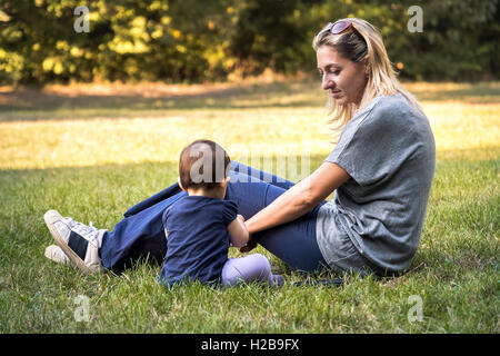 Une mère et son bébé nouveau-né fils assis dans l'herbe au parc passer du temps en famille dans un jardin Banque D'Images