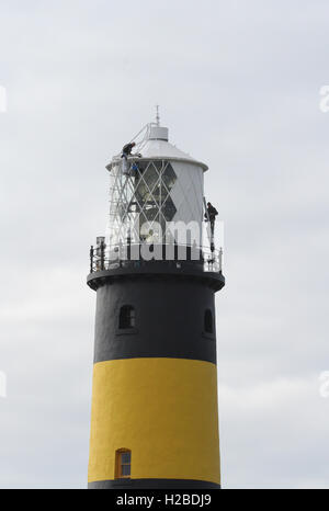 Peintres industriels travaillant en hauteur dans un environnement inhabituel tout en peignant un phare dans le comté de St John's point, en Irlande du Nord. Banque D'Images