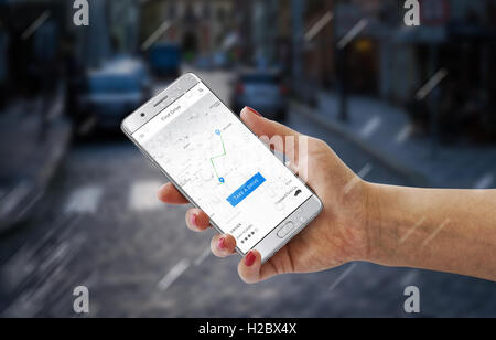 Voitures pilote app sur smartphone moderne dans femme la main. Rue de la ville en arrière-plan. Banque D'Images