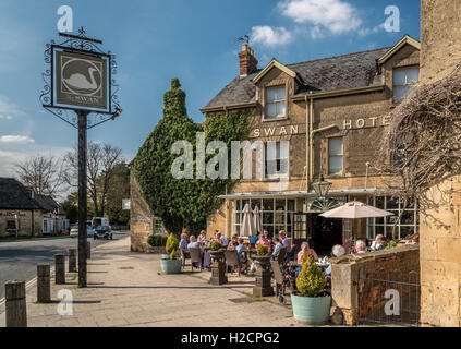 Les personnes bénéficiant d'un début de soirée verre au soleil en face d'un pub typique de village dans la région des Cotswolds. Banque D'Images