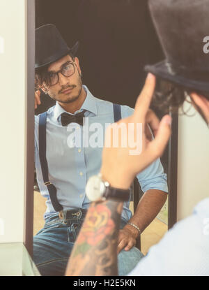 Portrait de jeune femme brune l'Homme à lunettes, chapeau, nœud papillon, bretelles et une chemise en se regardant dans un miroir. Look Vintage Banque D'Images