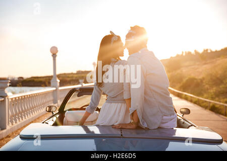 Happy young couple sitting et embrasser dans cabriolet on sunset Banque D'Images