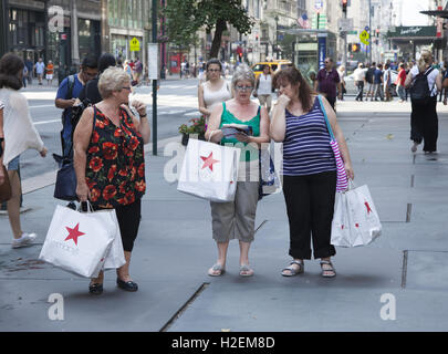 Tous les trois femmes avec Macy's shopping sur la 5e Avenue à Manhattan. New York City consulting une brochure touristique pour plus d'informations où aller. Banque D'Images