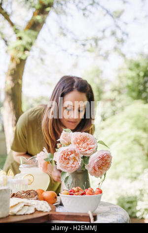 Femme debout à une table dans un jardin, d'un vase de roses et un bol de cerises. Banque D'Images