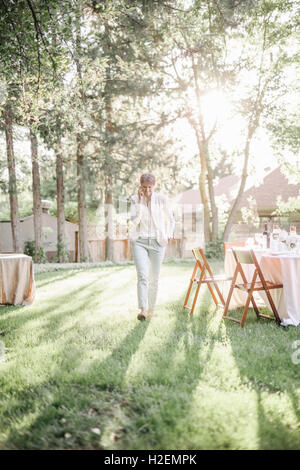 Femme debout dans un jardin ensoleillé, en parlant à son téléphone mobile. Banque D'Images