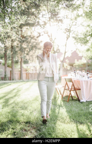 Femme debout dans un jardin ensoleillé, en parlant à son téléphone mobile. Banque D'Images