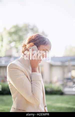 Femme debout dans un jardin ensoleillé, en parlant à son téléphone mobile. Banque D'Images