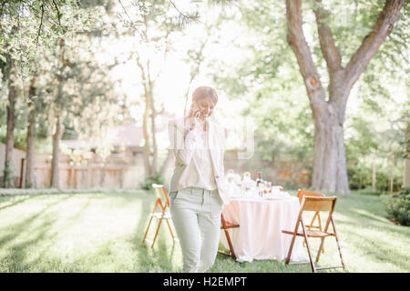 Femme debout dans un jardin ensoleillé, en parlant à son téléphone mobile. Banque D'Images