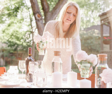 Femme blonde la définition d'une table dans un jardin, des bougies et des vases avec des roses roses. Banque D'Images