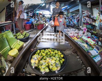 Samut Songkhram, Samut Songkhram, Thaïlande. 27 Sep, 2016. Une mère et sa fille à pied le long des rails, passé un stand vendant des limes dans le marché de la gare à Samut Songkhram. Le train de l'Baen Laem à Samut Songkhram (Mae Khlong) récemment repris du service. La piste de 33 kilomètres a été fermée pour réparation pendant près d'un an. Dans Samut Songkhram, le train passe sur le marché. Tirer sur leurs stands des fournisseurs à l'écart et les gens sortir de la façon que le train passe à travers le marché. C'est l'une des plus célèbres stations de train en Thaïlande et est devenu un important touris Banque D'Images