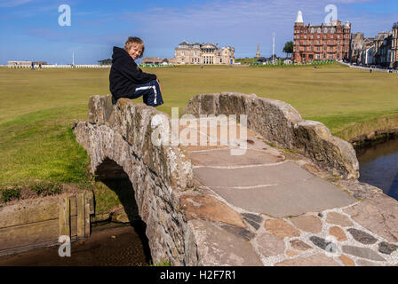 Un jeune garçon est assis sur le Swilken Bridge, à la maison du golf Le Royal and Ancient Golf Club. Saint Andrews Fife en Écosse. Banque D'Images