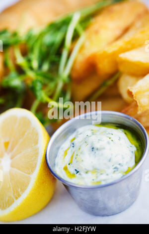 Chips cuits sur une assiette et napper avec la sauce tartare et une coupe citron . Banque D'Images