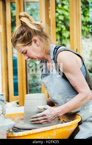 Une femme d'argile de potier sur un tour de potier dans son atelier. Banque D'Images