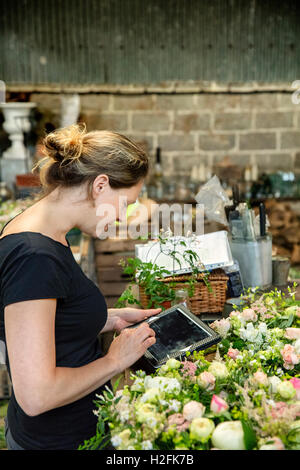 Une femme à l'aide d'une tablette numérique fleuriste dans un atelier. Banque D'Images