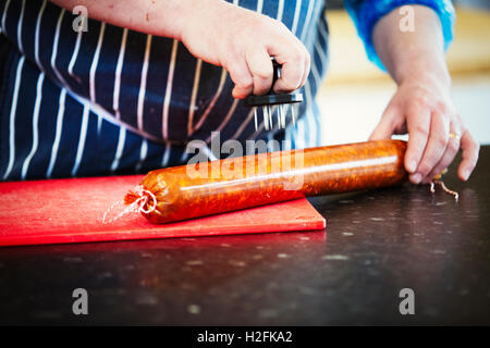 Portrait d'un boucher le port d'un tablier bleu à rayures , piquer des trous dans le boîtier d'un chorizo. Banque D'Images