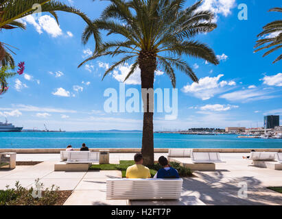 Les gens s'asseoir à l'ombre des palmiers et de profiter du soleil tout en donnant sur port de Split de la riva. Banque D'Images