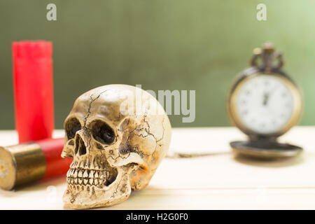 Crâne humain reposant sur un plancher en bois et un fusil de chasse rouge shell avec montres anciennes dans l'arrière-plan. Banque D'Images