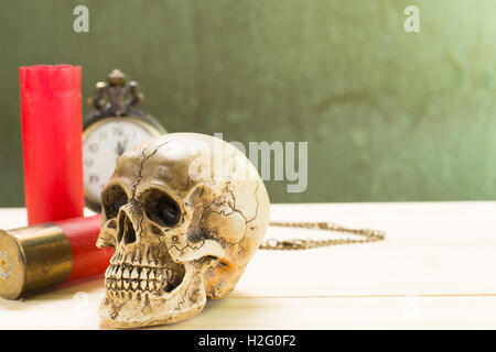 Crâne humain reposant sur un plancher en bois et un fusil de chasse rouge shell avec montres anciennes dans l'arrière-plan. Banque D'Images