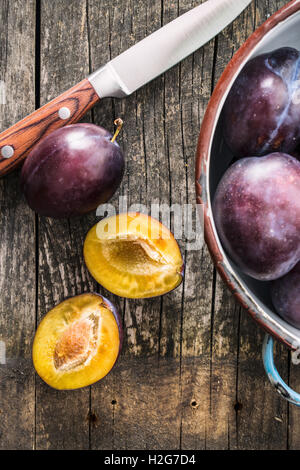 Les prunes mûres coupées en deux et le couteau sur la vieille table en bois. Vue d'en haut. Banque D'Images