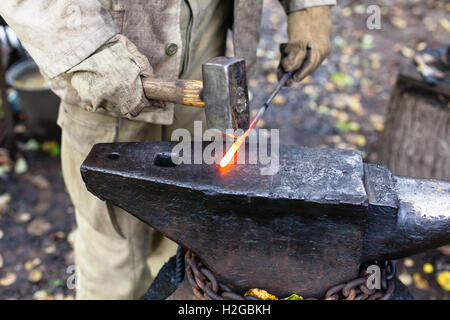 Blacksmith hammering hot tige acier sur enclume dans l'air extérieur forge rurale Banque D'Images