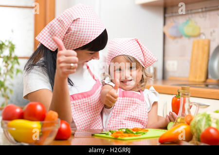 Heureuse mère et fille avec des légumes frais showing Thumbs up geste. Tourné dans la cuisine Banque D'Images