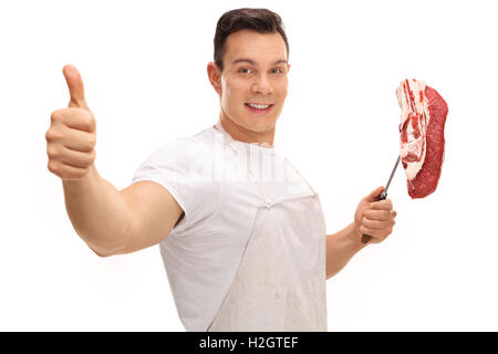 Cheerful butcher donner un pouce vers le haut et tenant une fourche à l'aide d'un steak isolé sur fond blanc Banque D'Images