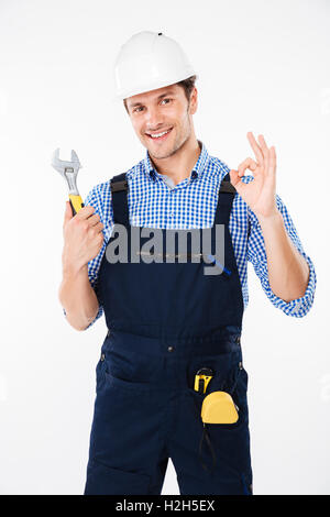 Cheerful young man builder in hard hat holding clé et montrant ok sign Banque D'Images