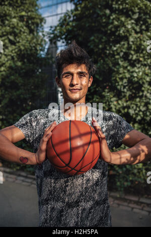 Portrait de jeune joueur de basket-ball avec une balle. Les joueurs de streetball sur cour extérieure looking at camera avec balle en ha Banque D'Images