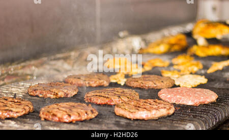 Burgers de boeuf et des ailes de poulet et sur une flamme grill grésillant Banque D'Images