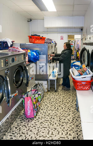 Femme à l'aide d'un lave-linge en libre-service dans une laverie. Banque D'Images