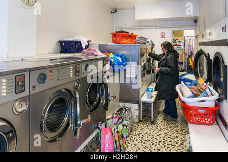 Femme à l'aide d'un lave-linge en libre-service dans une laverie. Banque D'Images