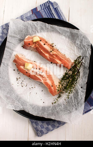 Bandes de porc avec du poivre concassé, le thym et l'ail avec du papier de cuisine blanche sur une plaque Banque D'Images