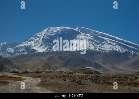 Yourtes touristiques en béton sur le bord du lac Karakul avec Mustagh Ata montagne derrière, la Province du Xinjiang, Chine Banque D'Images