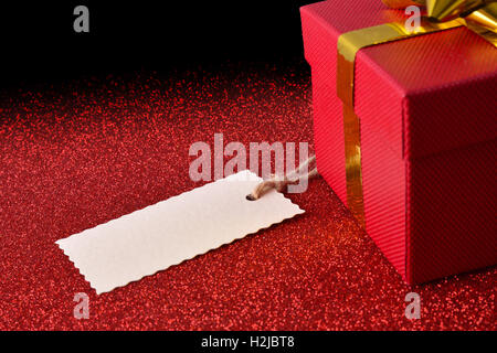 Boîte cadeau rouge et or blanc avec ruban rouge vif sur tag table texturé et dégradé en noir. Vue élevée. Banque D'Images