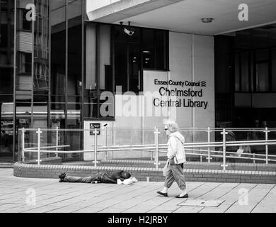 L'homme sans-abri dormir dehors pour le conseil du comté de Chelmsford Bibliothèque dans l'été de 2016 dans l'Essex en Angleterre comme une personne marche Banque D'Images