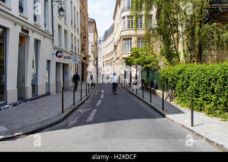 Femme circuler à bicyclette sur l'une des rues dans le quartier du Marais de Paris. Nous voyons des gens marcher et styles architecturaux français en bu Banque D'Images