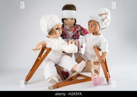 Trois poupées assis, des bandages sur la tête, la jambe d'une attelle, béquilles, eye patch, bras et l'épaule bandage, NECK BRACE, fond blanc Banque D'Images