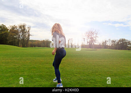 Blonde girl jumping with joy sur fond de pelouse verte hotspot ensoleillée Banque D'Images