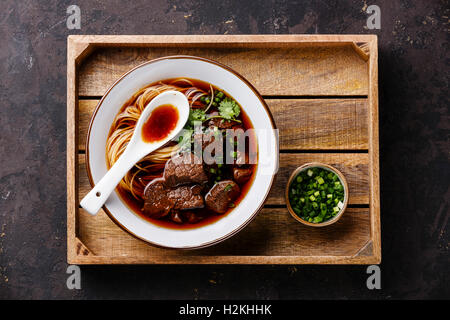 Nouilles asiatiques dans un bouillon de Bœuf mijotés avec en plateau en bois sur fond sombre Banque D'Images