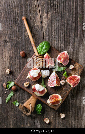 Figues fraîches tranches de fromage ricotta, de feuilles de basilic, de noisette et de miel miel de balancier sur petite planche à découper en bois foncé dessus Banque D'Images