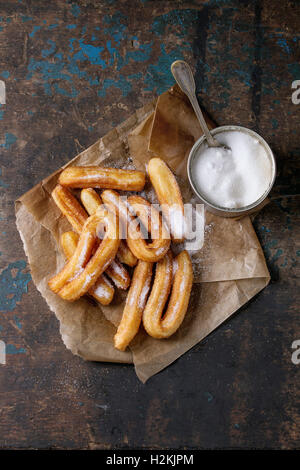 Traiter les churros espagnole traditionnelle avec du sucre granulé, servi sur du papier sulfurisé avec boite de conserve de sucre plaque ovale sur dark woode Banque D'Images