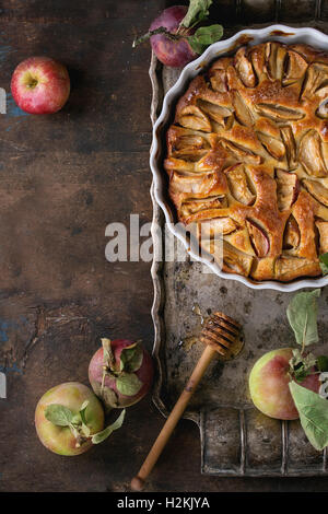 Tarte gâteau pommes maison blanche en forme de céramique sur le plateau métallique vintage avec des pommes fraîches avec des feuilles et de miel sur bac en bois foncé Banque D'Images