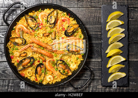 La Paella espagnole sur une table en bois foncé avec du citron sur une plaque en ardoise Banque D'Images