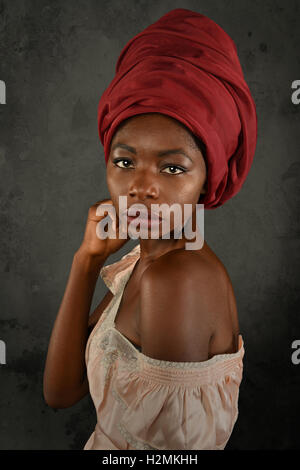 Jeune femme africaine avec turban rouge sur fond gris Banque D'Images