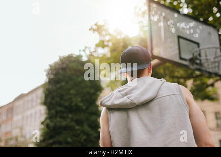 Vue arrière Vue d'un joueur de streetball debout sur un terrain de basket-ball en plein air sur une journée d'été. Banque D'Images