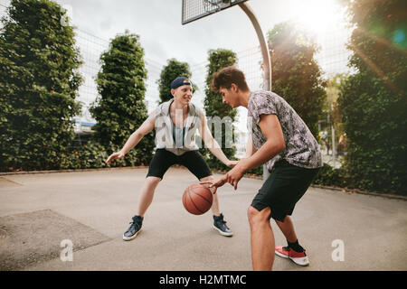 Adolescents jouant au basket-ball sur une cour et d'avoir du plaisir. Young man dribbling basketball avec ami bloquer. Banque D'Images