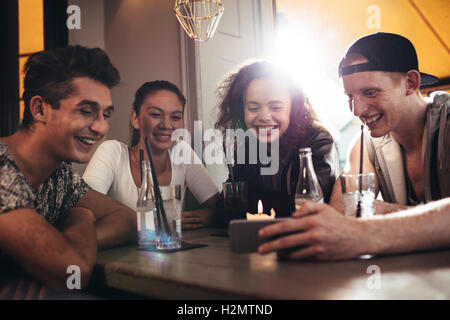 Groupe d'amis assis ensemble dans un cafe looking at mobile phone et souriant. Jeune homme montrant quelque chose à ses amis sur h Banque D'Images